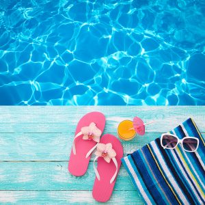 Summer Holidays in Beach Seashore. Summer drinks. Summer rest. Fashion accessories summer flip flops, hat, sunglasses on bright turquoise board near the pool